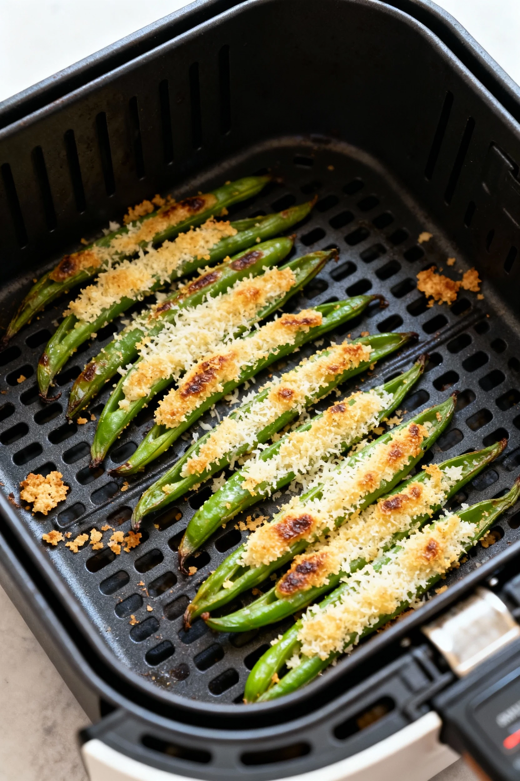 Cooking process: air fryer basket with green beans in a single layer mid-cook, visible blistering and light golden Parme